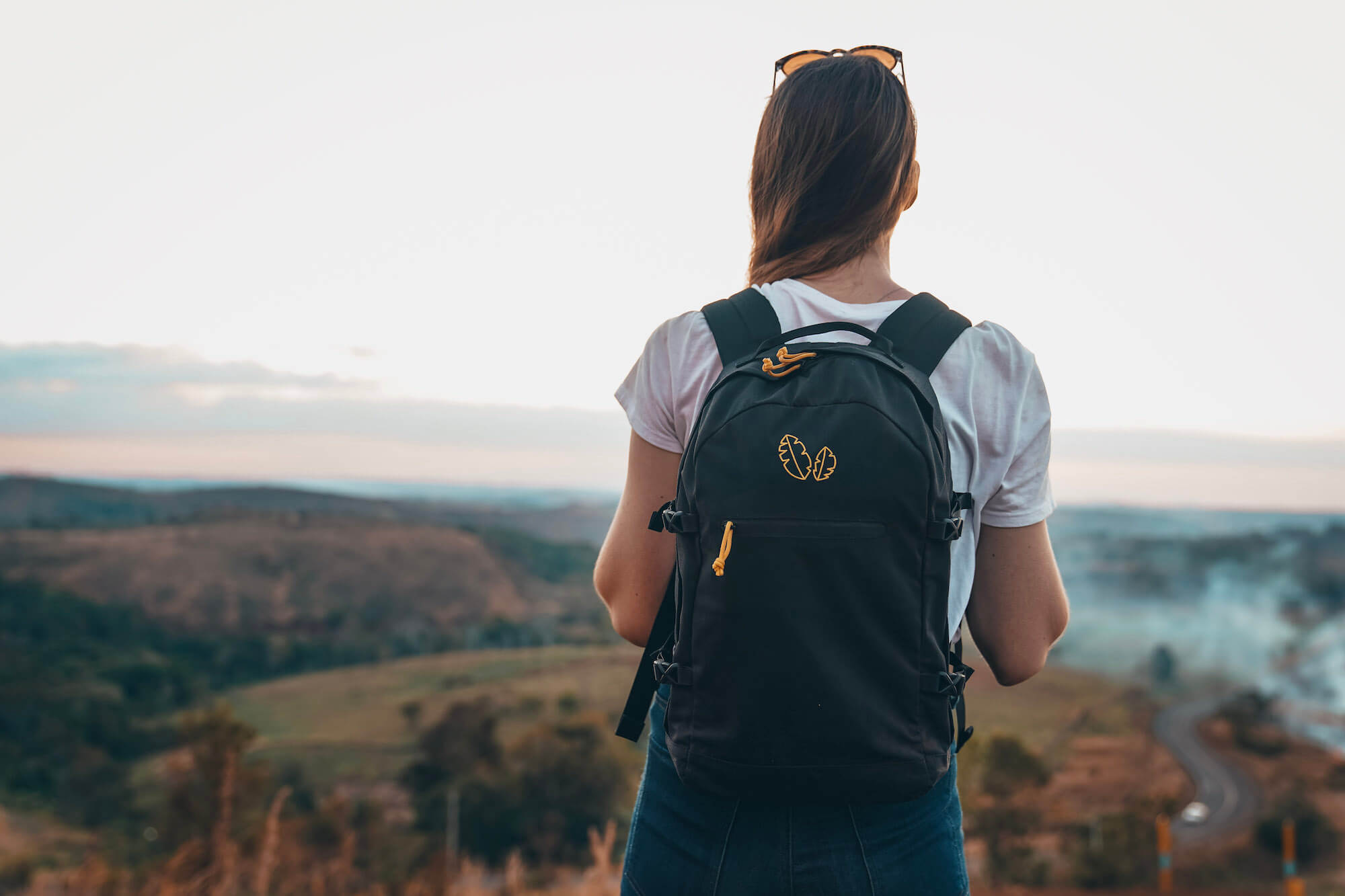 Girl wearing backpack looks out at sunset in Mondulkiri